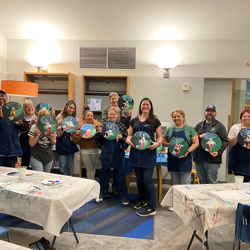 A group of adults proudly displaying their finished artwork done during a Paint 'N Sip class at the Glenn A Jones MD Memorial Library adult programs