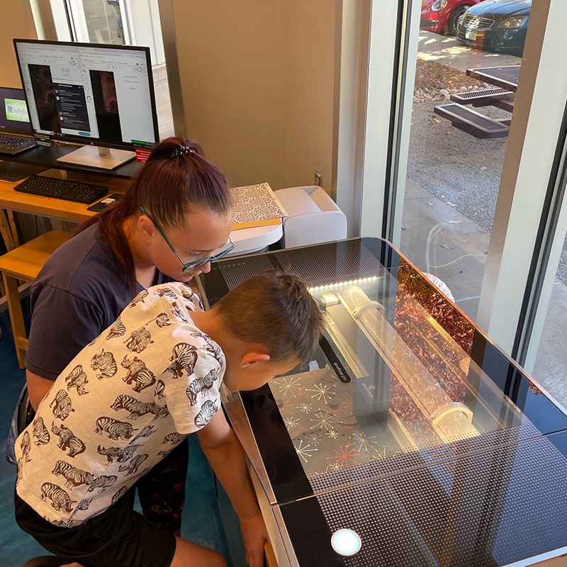 A mother and son use the 3-D printer at the Glenn A Jones MD Memorial Library Makerspace