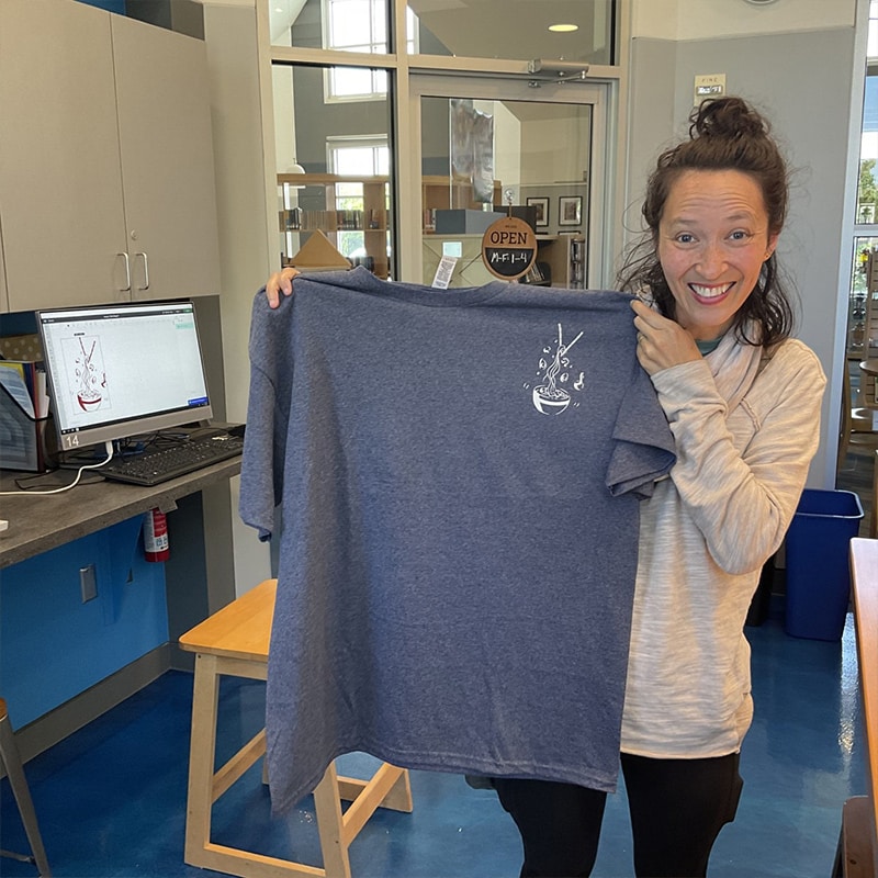 A woman uses the t-shirt press to create a custom t-shirt at the Glenn A Jones MD Memorial Library Makerspace