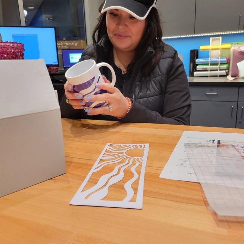 A woman decorates a coffee mug using the Cricut machine at the Glenn A Jones MD Memorial Library Makerspace