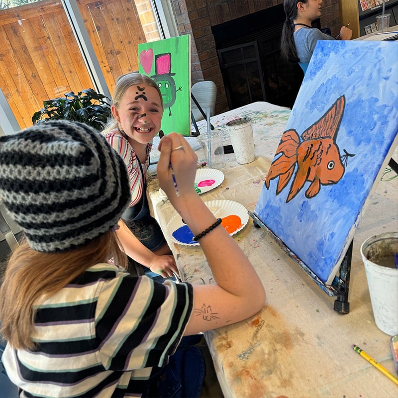 Two girls working on a painting at the Glenn A Jones MD Memorial Library Paint N' Sip Teen Programs